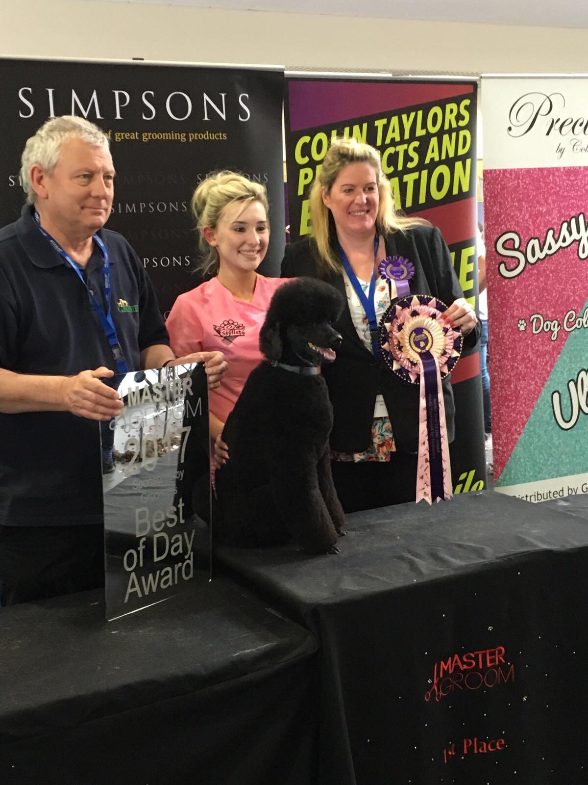Receiving a Best of Day award with a black poodle at a grooming show